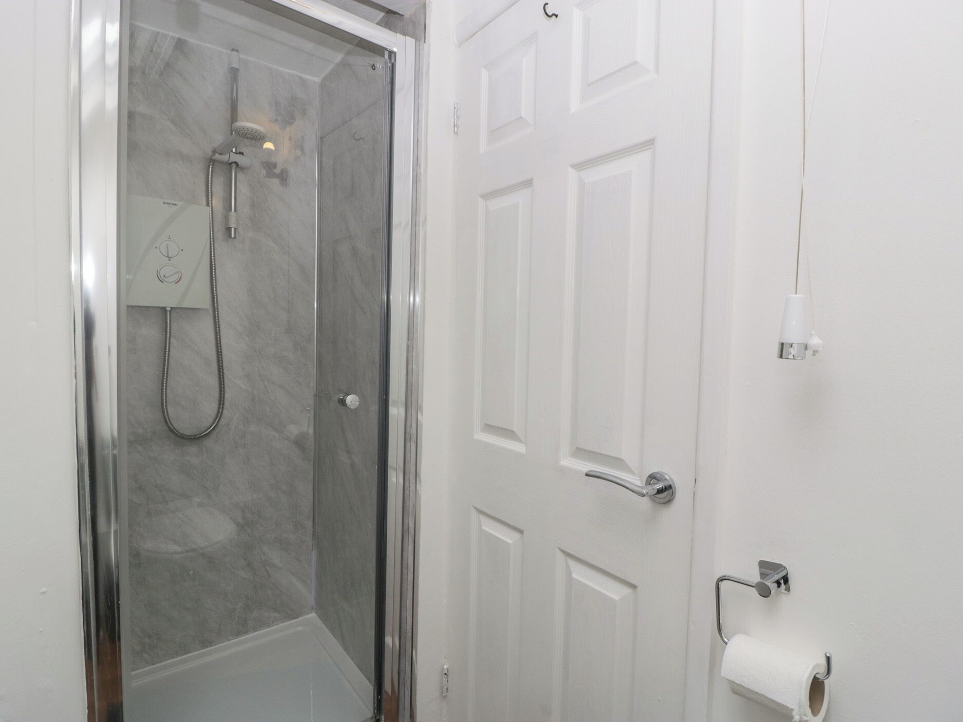 Une salle de bain avec une douche à parois de verre, une porte blanche et un porte-rouleau de papier toilette.