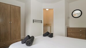 Een slaapkamer met een grote houten garderobe, een bed met wit beddengoed en een kleine spiegel aan de muur.