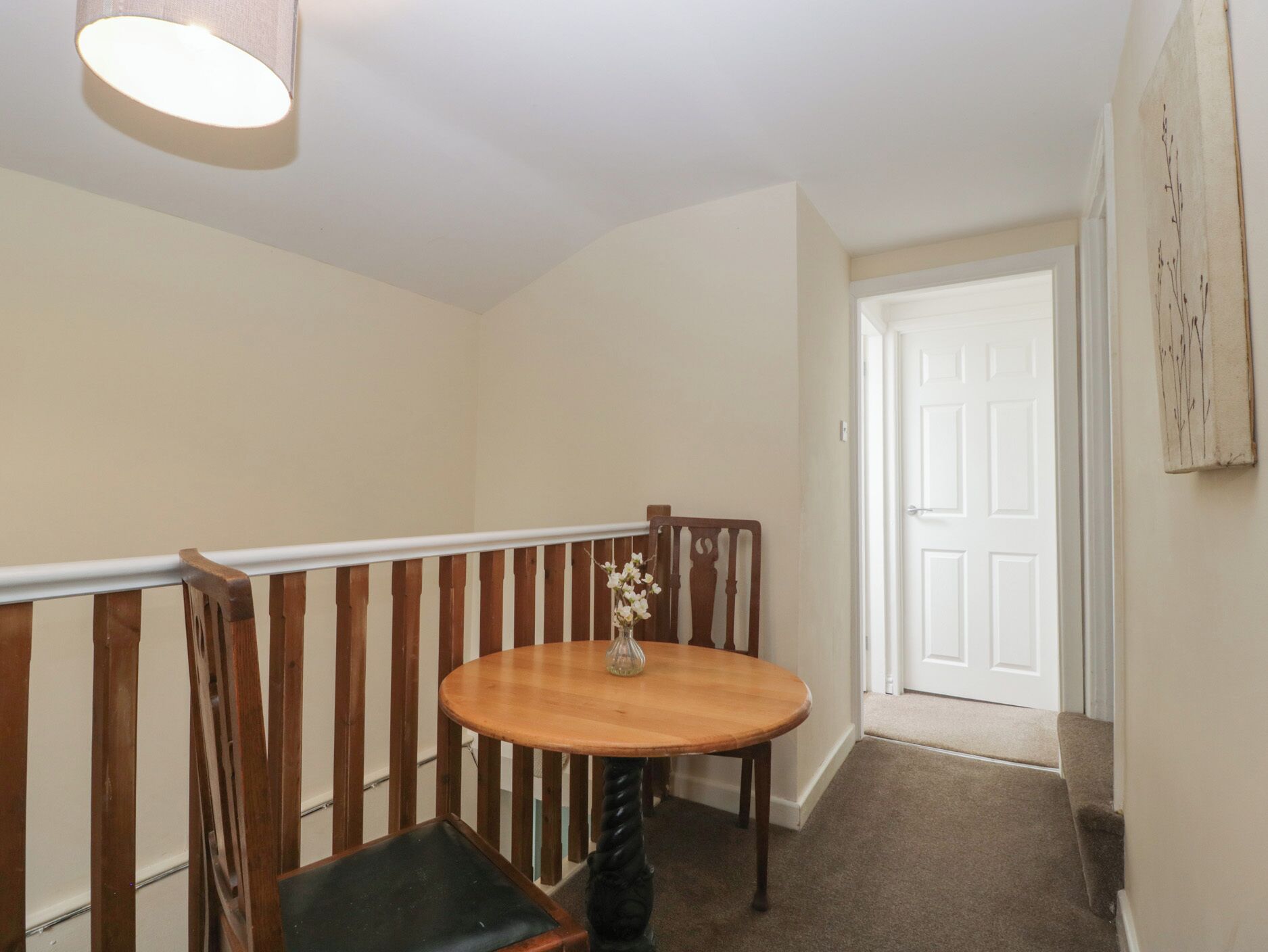 A hallway with a wooden chair, a small round table with a vase, and a white door at the end.