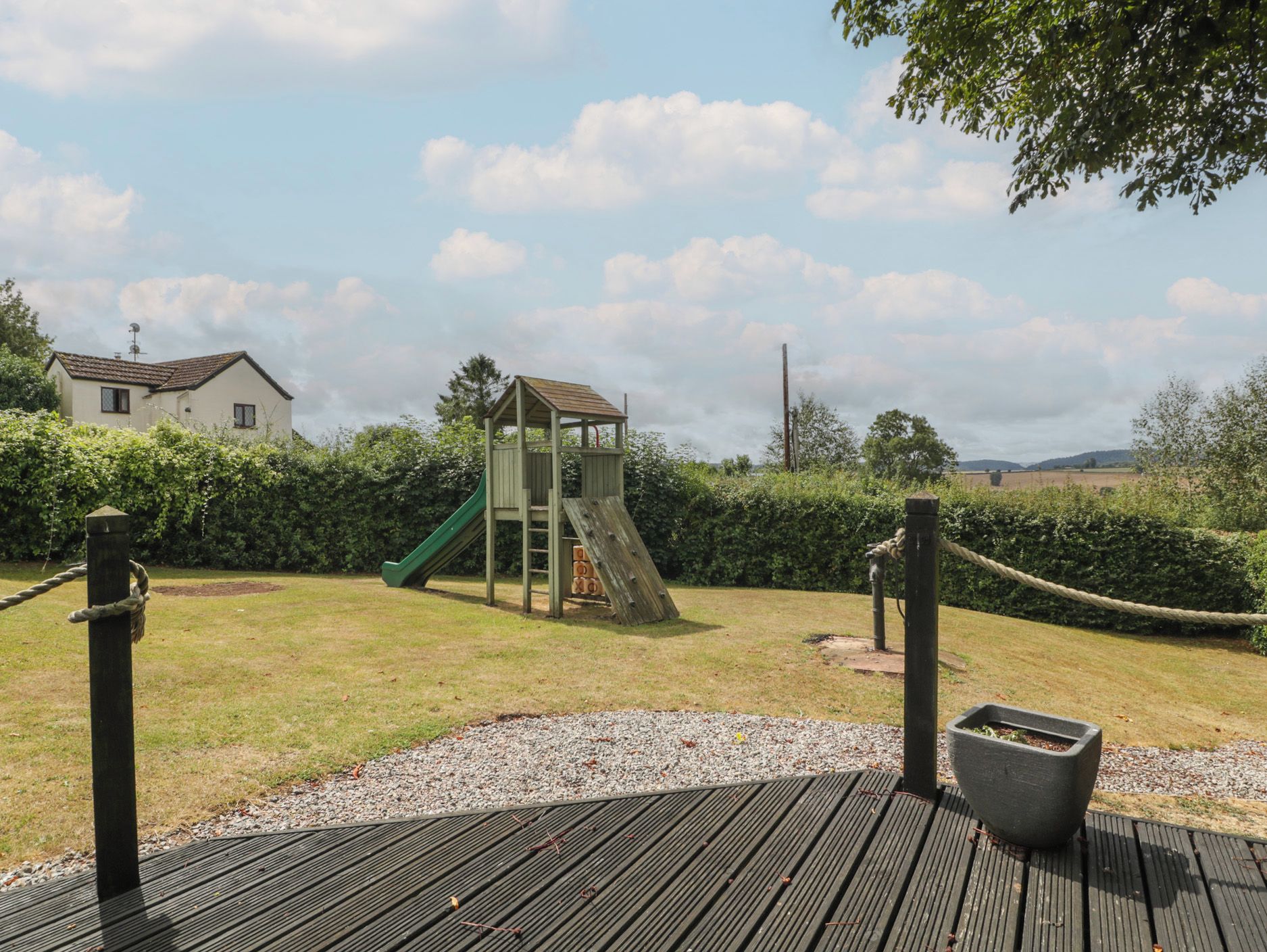 A playground with a slide and climbing structure, surrounded by a grassy area and a wooden deck.