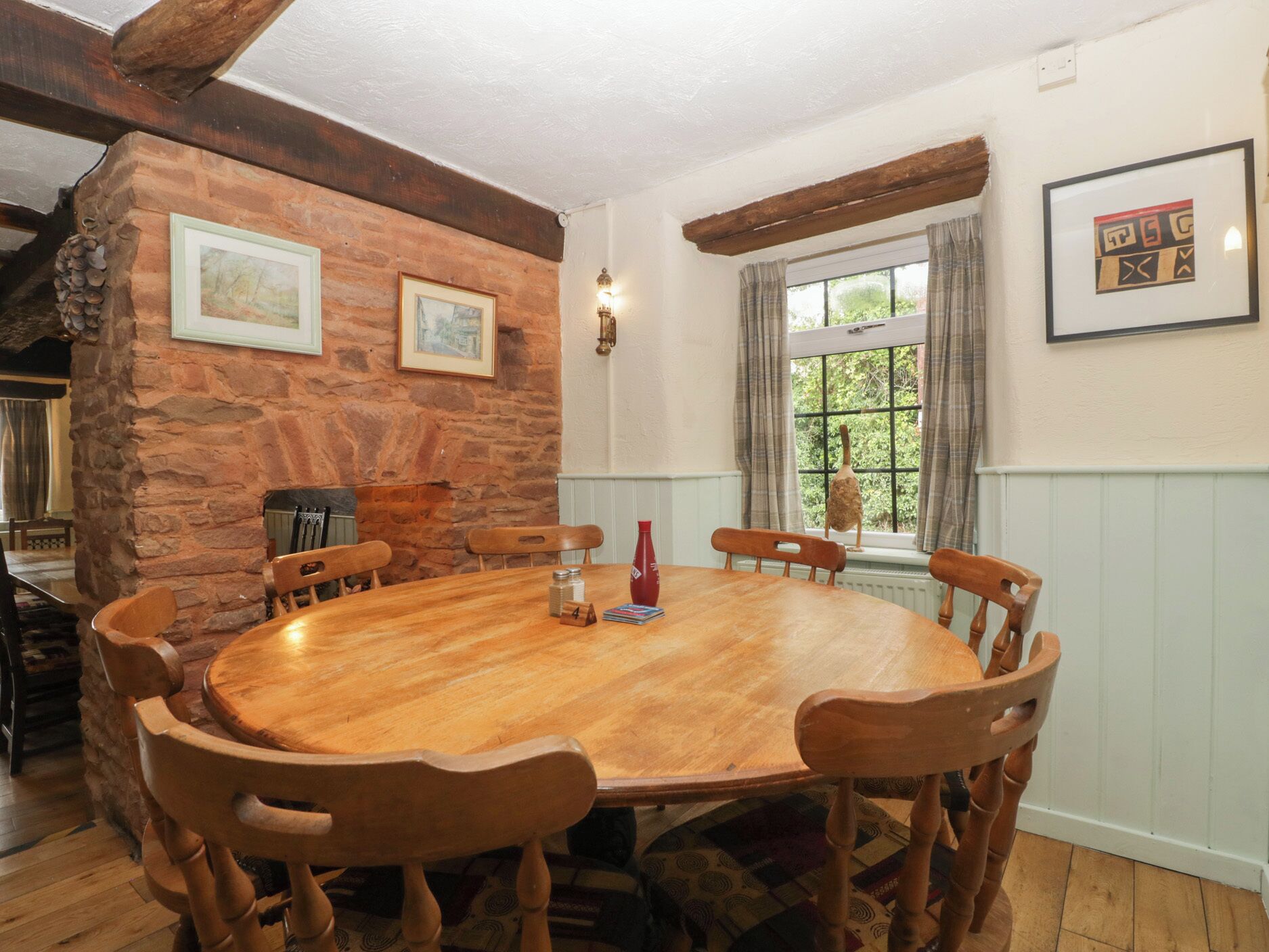 A dining room with a wooden table and chairs, stone wall, and a window with curtains.