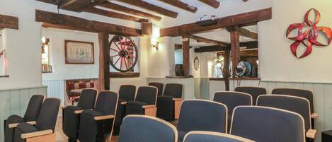 A room with multiple seating areas, wooden beams on the ceiling, a dartboard, and a wall with a decorative item.