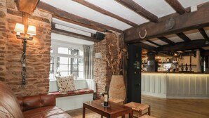 Een gezellig pubinterieur met een stenen muur, houten balken, een bar, lederen zitplaatsen en een raam met uitzicht.