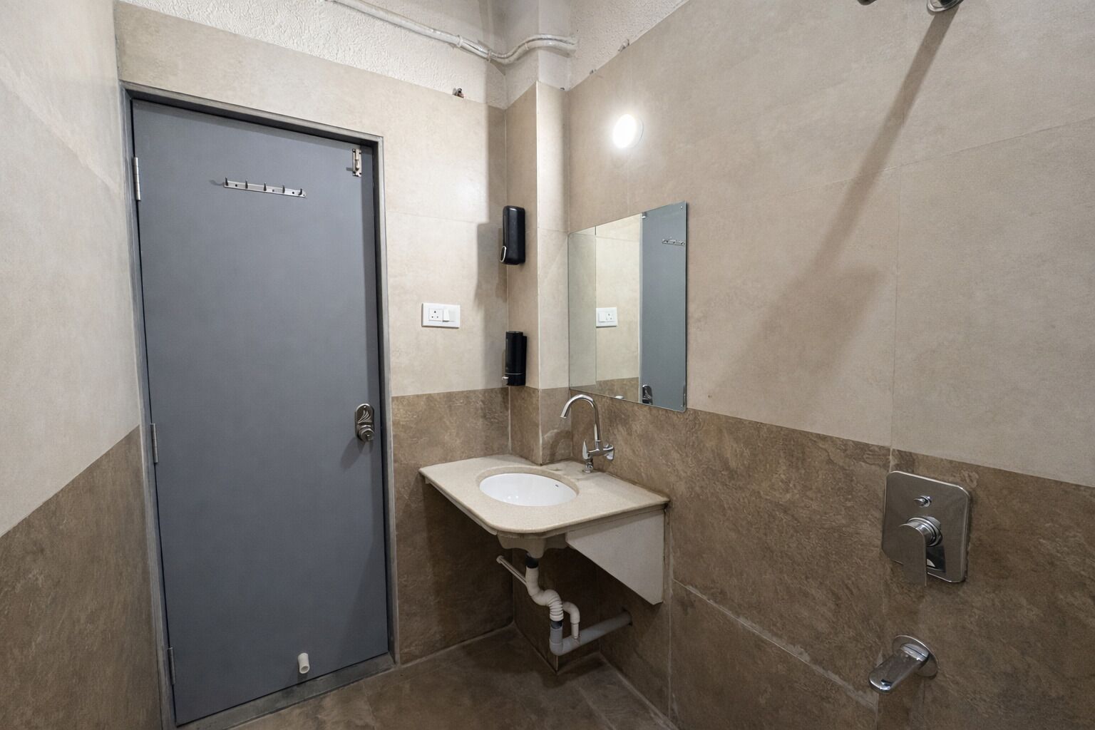 A bathroom with a grey door, a sink with a mirror, and a towel rack.