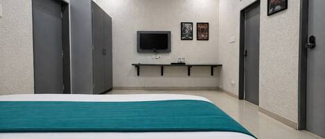 A hotel room with a bed, a TV mounted on the wall, and a shelf with glasses.