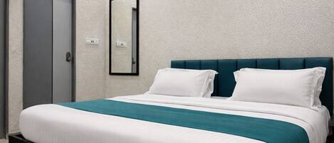 A hotel room with a bed, a door, and a wall-mounted mirror.