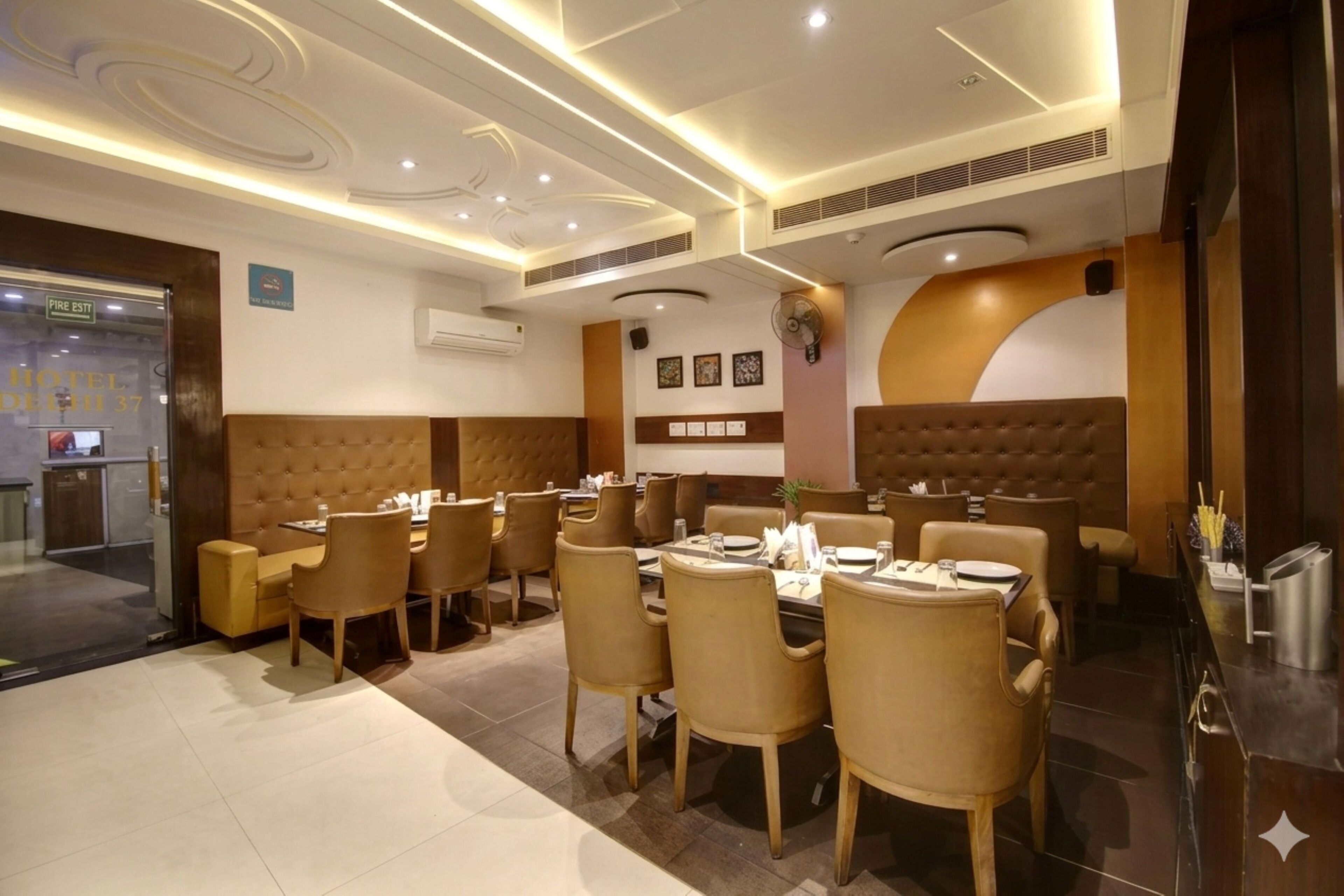 A hotel dining area with round tables, cushioned chairs, and a modern ceiling design.