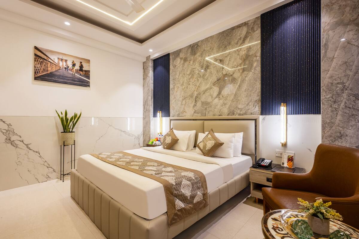 Una habitación de hotel moderna con una cama grande, una zona de estar, una mesita de noche y un televisor montado en la pared.