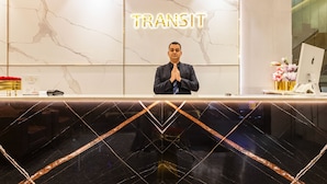 Un comptoir d’accueil avec un mur en marbre et un panneau néon sur lequel on peut lire « TRANSIT ».