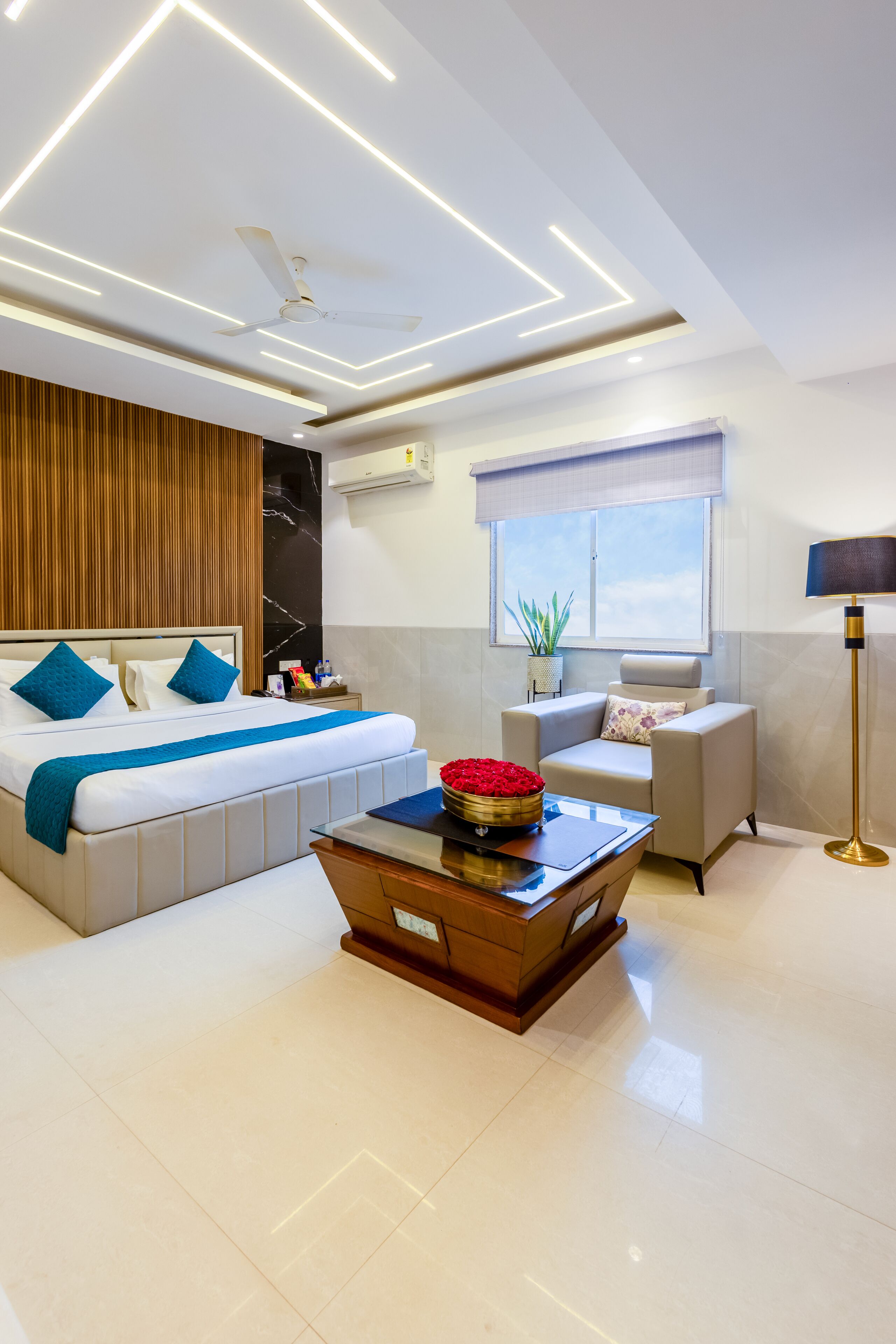 A modern hotel room with a large bed, a desk, a chair, a ceiling fan, and a window with a view.