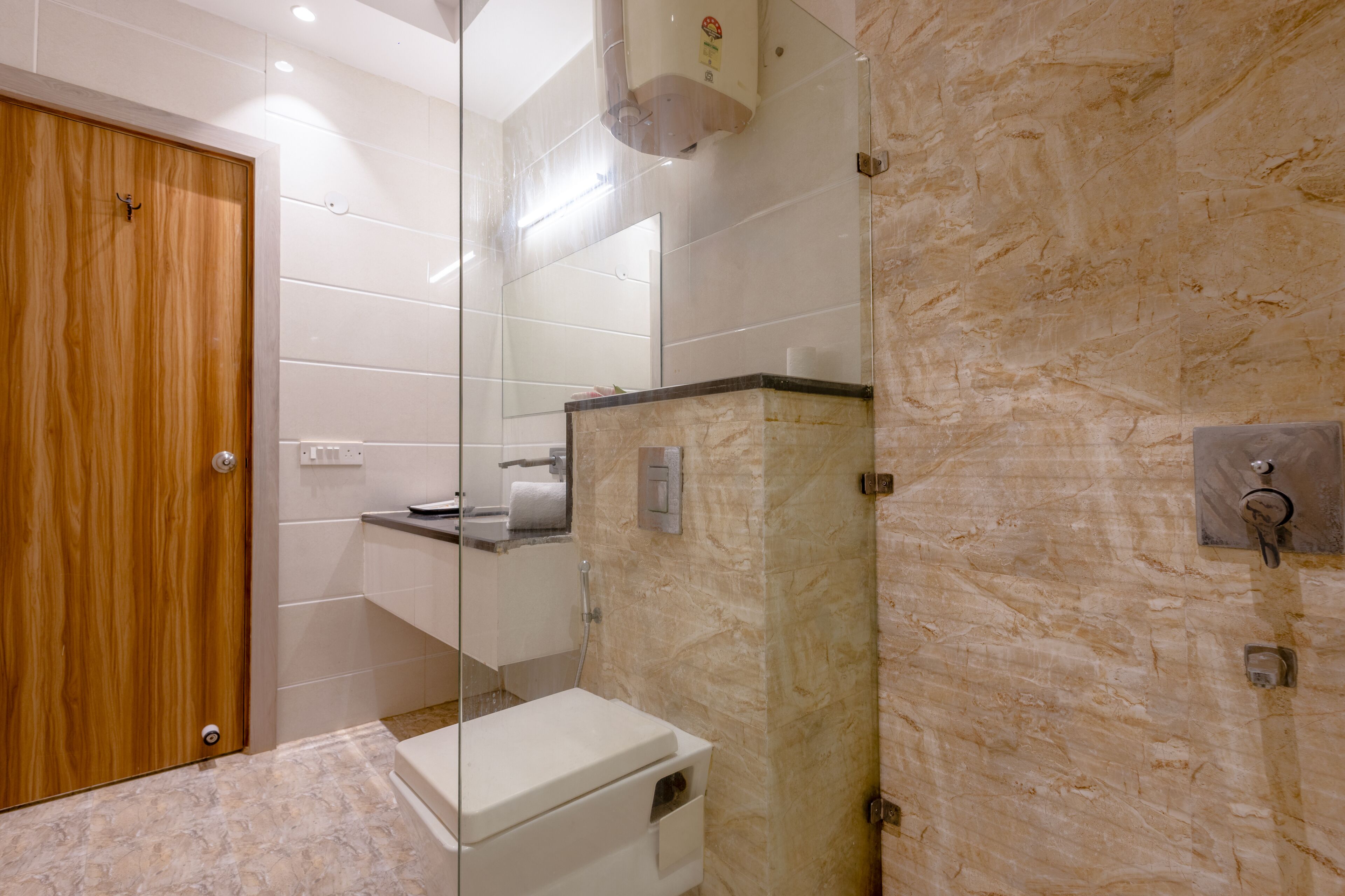 A modern bathroom with a wooden door, a white toilet, a sink with a mirror above it, and a marble wall.