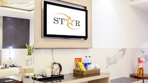 Un hall d’hôtel moderne avec un comptoir d’accueil, un petit réfrigérateur, une machine à café et un écran de télévision affichant le mot « STAR ».