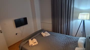 Quarto de hotel com cama, televisão de tela plana, luminária de teto, ar condicionado e abajur.