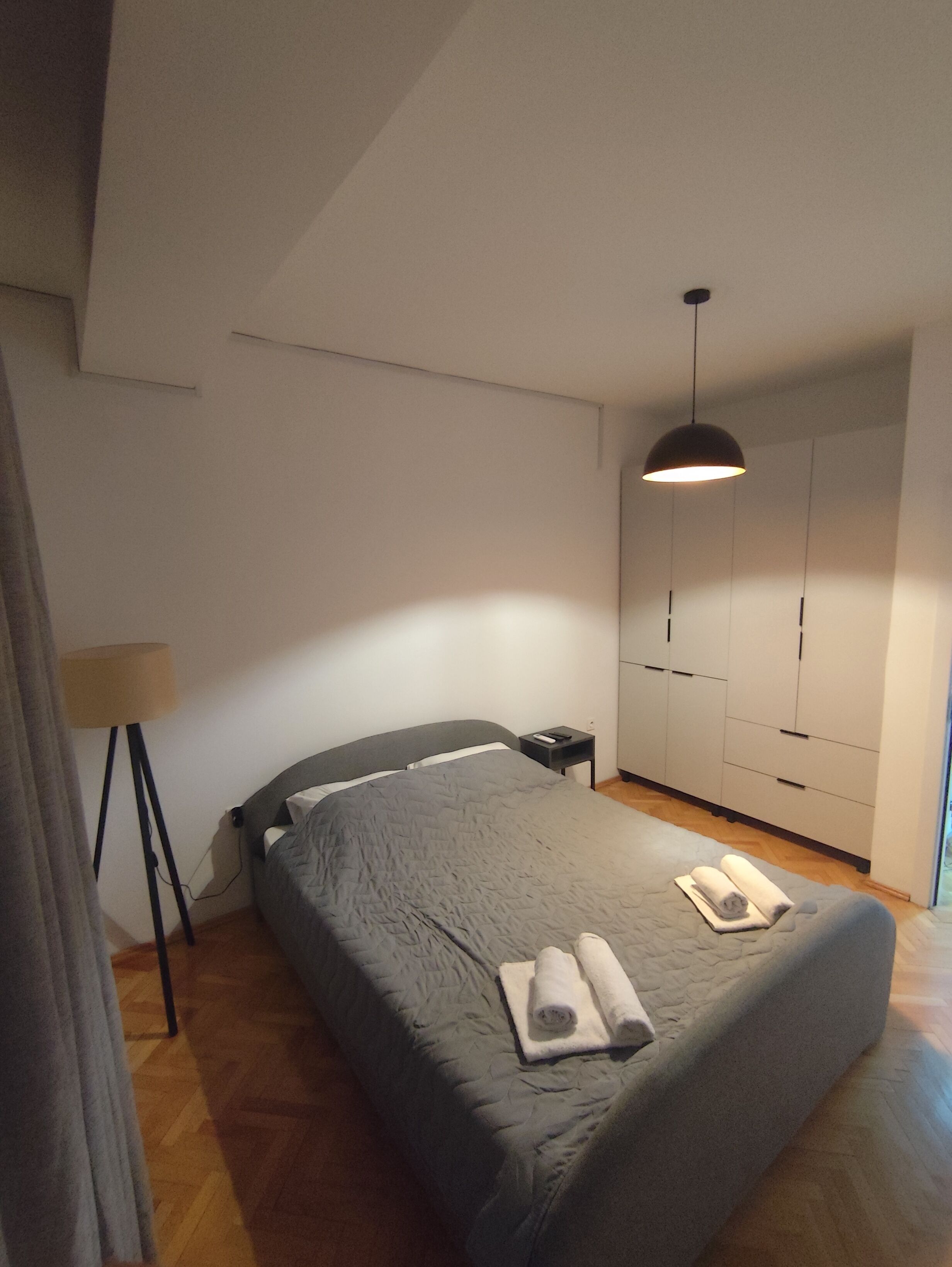 A bedroom with a bed, a bedside table, a lamp, and a wardrobe.