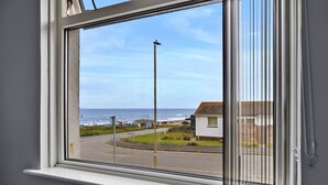 A window with a view of a coastal road, a street lamp, and a building with a red roof. - Sea Thrift at Widemouth Bay (Widemouth Bay)