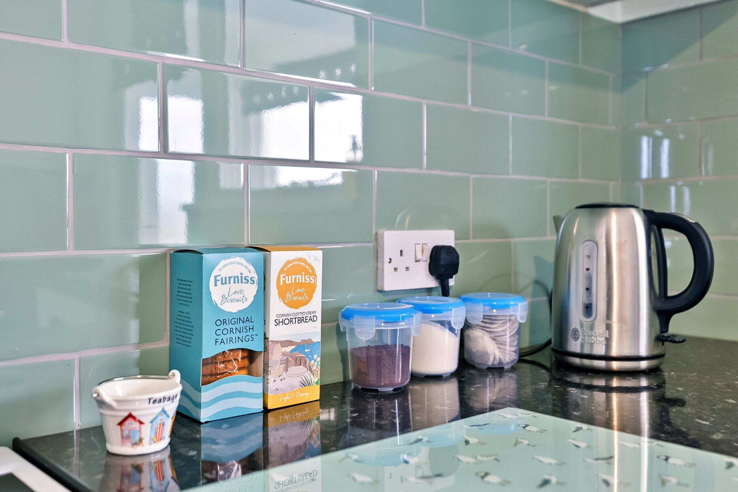 A kitchen counter with a box of Cornish Shortbread, a teapot, and containers of flour and sugar.