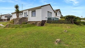 A single-story house with a white exterior, a front porch, and a small garden area with grass and flowers. - Sea Thrift at Widemouth Bay (Widemouth Bay)