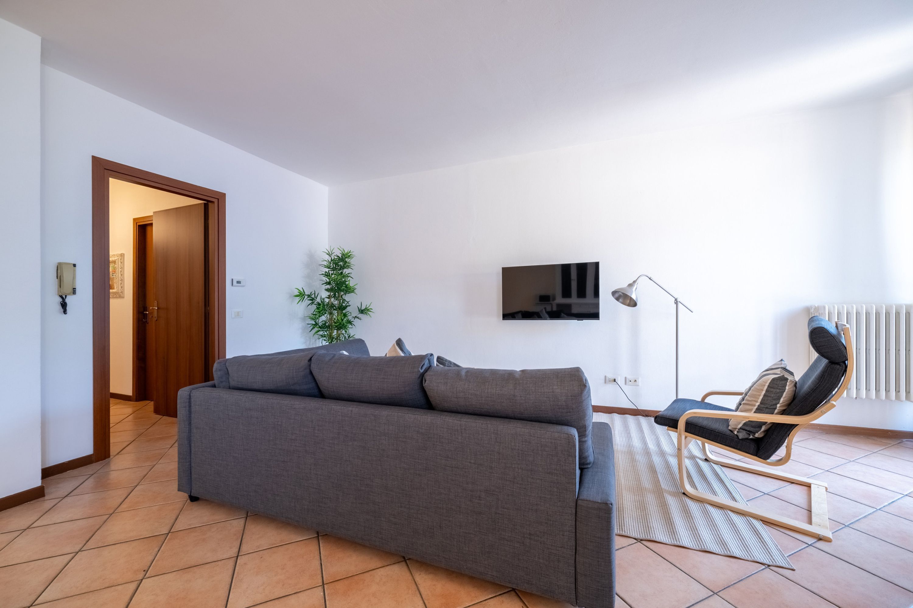 Una sala de estar con un sofá gris, una silla con marco de madera, un televisor y un radiador.
