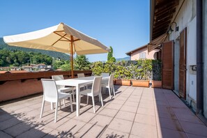 An outdoor patio with a table and chairs, a large umbrella, and potted plants. - Cascine Trilocale con Terrazza by Wonderful Italy (Bellagio)