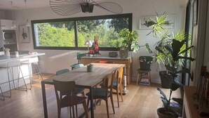 A modern kitchen with a dining area, large windows, and various plants. - 150 m² wooden family house with 3 terraces, close to the sea and surf spots! (Landunvez)