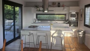 A modern kitchen with a central island, bar stools, a large window, and built-in appliances. - 150 m² wooden family house with 3 terraces, close to the sea and surf spots! (Landunvez)