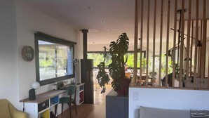 A modern living room with a large window, a dining area, and a kitchen. - 150 m² wooden family house with 3 terraces, close to the sea and surf spots! (Landunvez)