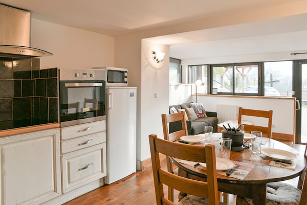 A kitchen with a microwave, oven, and refrigerator; a dining table with chairs; and a window with a view of the street.