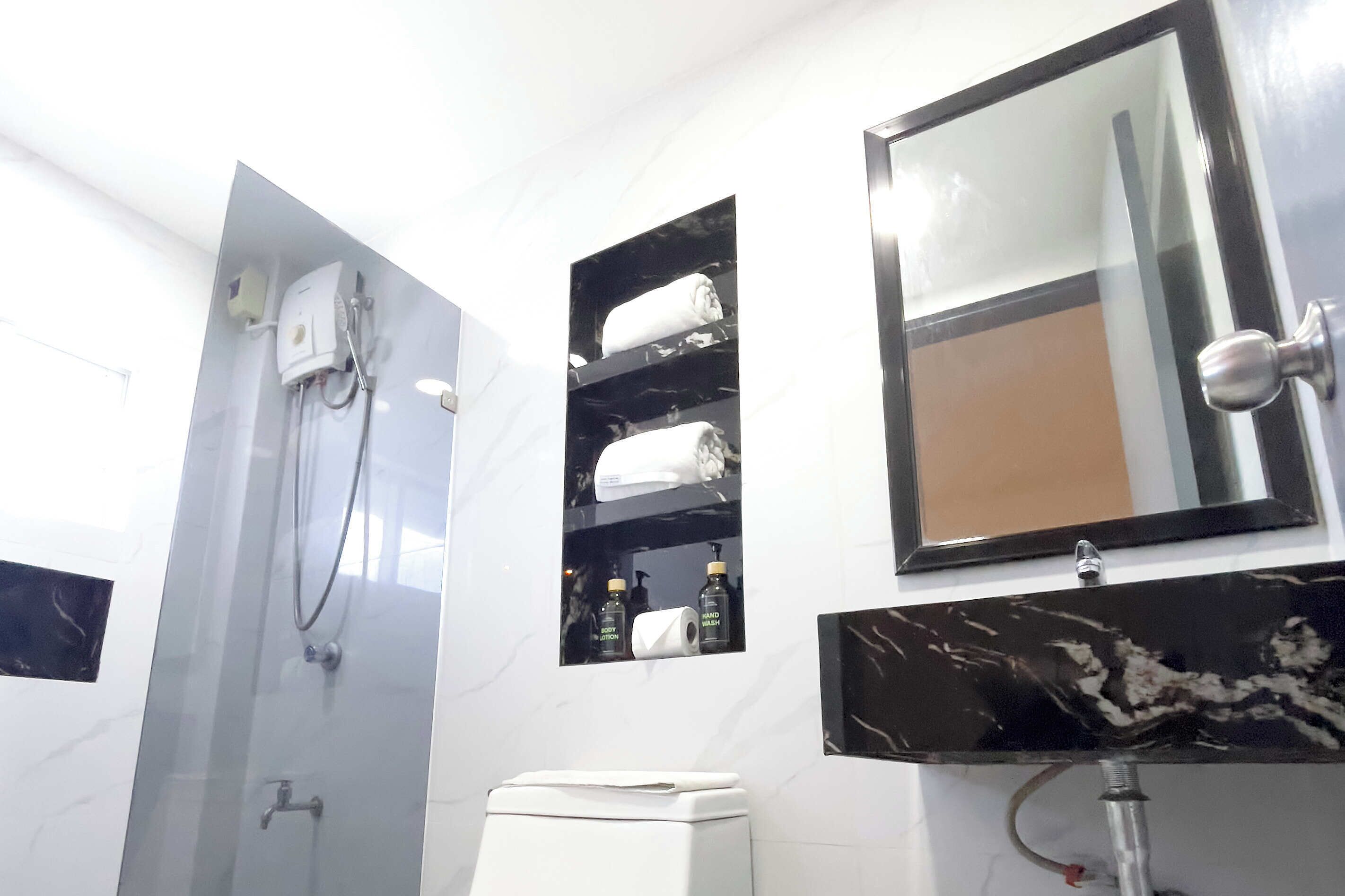 Un baño moderno con ducha envuelta en vidrio, inodoro blanco, lavabo de mármol y espejo sobre el lavabo.