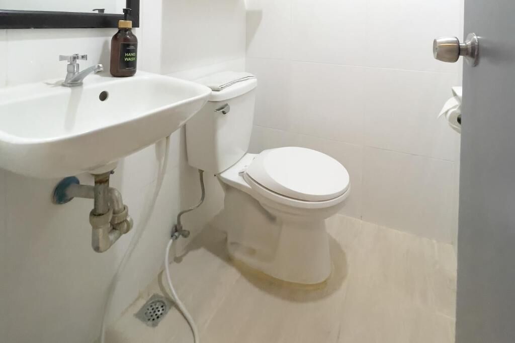 A small bathroom with a white sink, toilet, and a bottle of hand soap on the sink.
