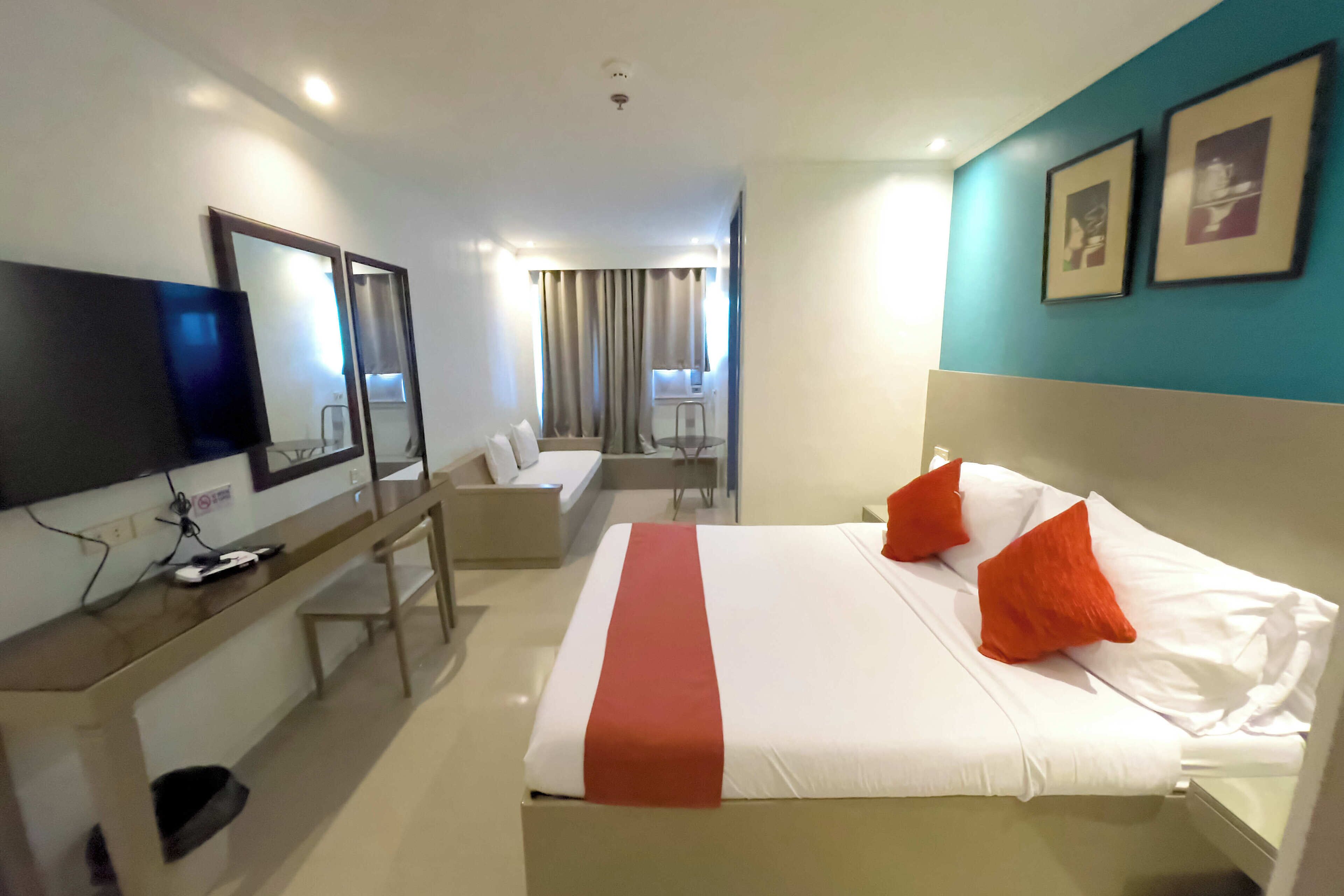 Habitación de hotel con cama, escritorio, silla, televisor y ventana con cortinas.