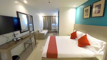 Habitación de hotel con cama, escritorio, silla, televisor y ventana con cortinas.