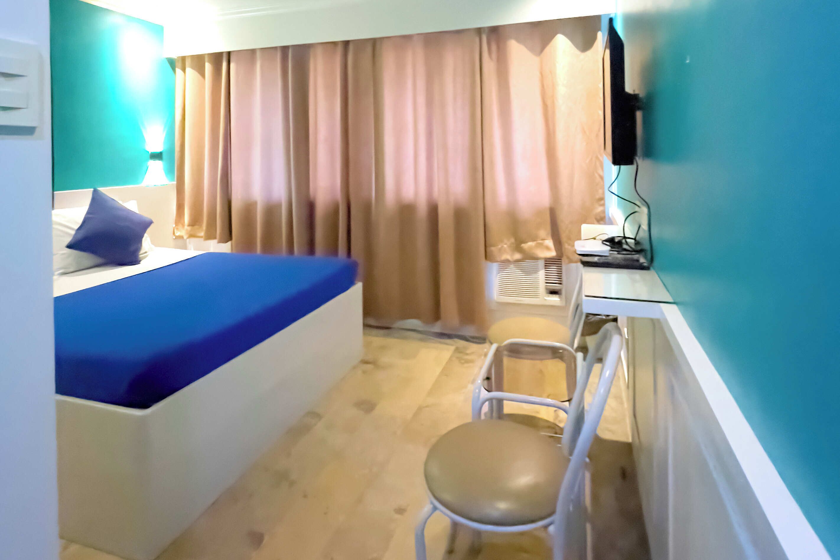 A hotel room with a bed, a desk, a chair, and a television.