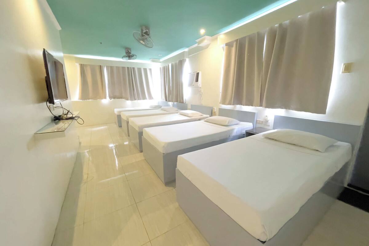 A hotel room with three beds, a TV, and a ceiling fan.