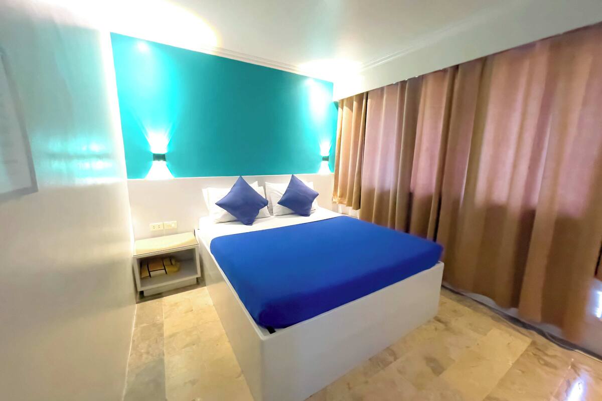 A hotel room with a bed, a nightstand, and a wall-mounted lamp.
