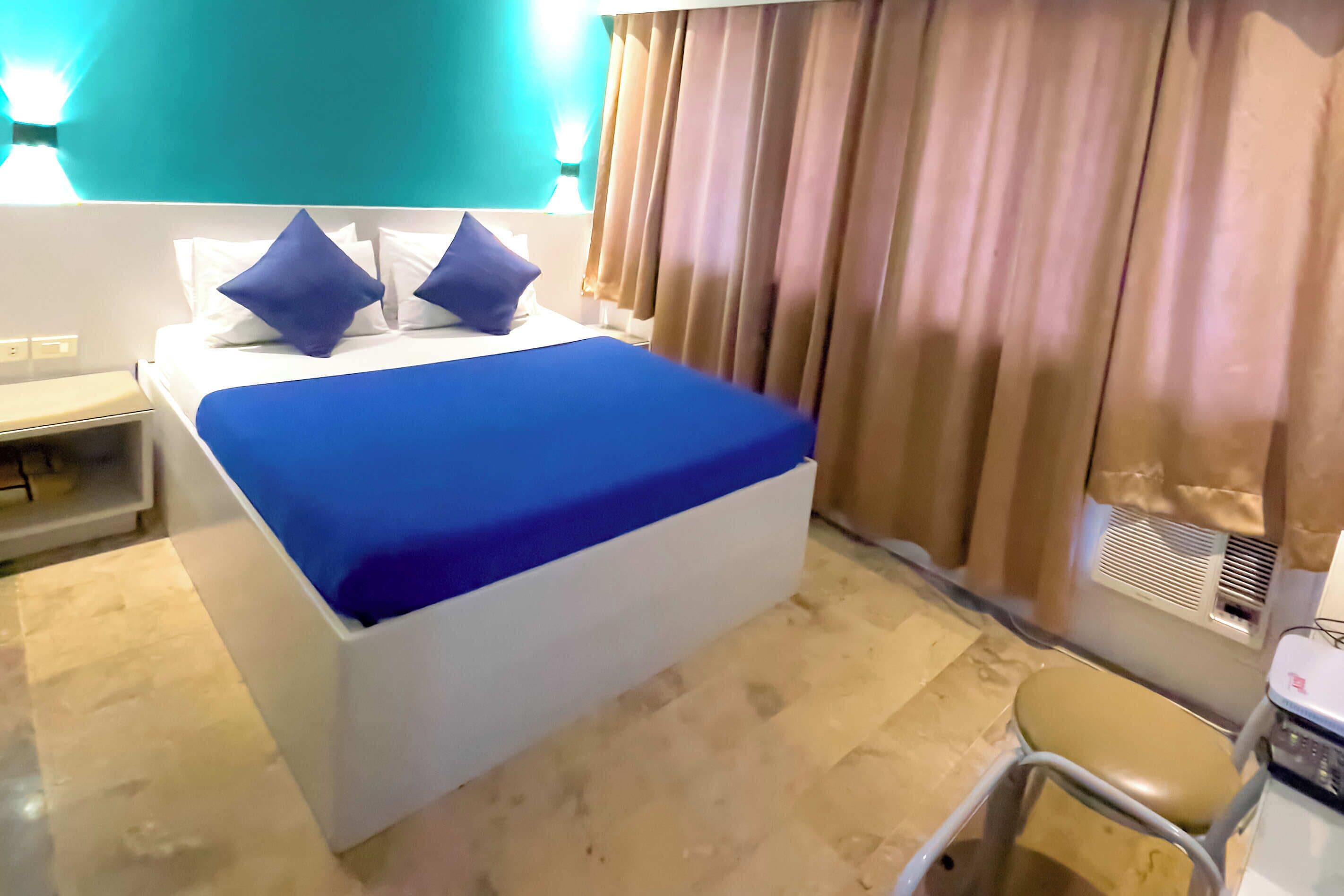 A hotel room with a bed, a desk, a chair, and a window with curtains.