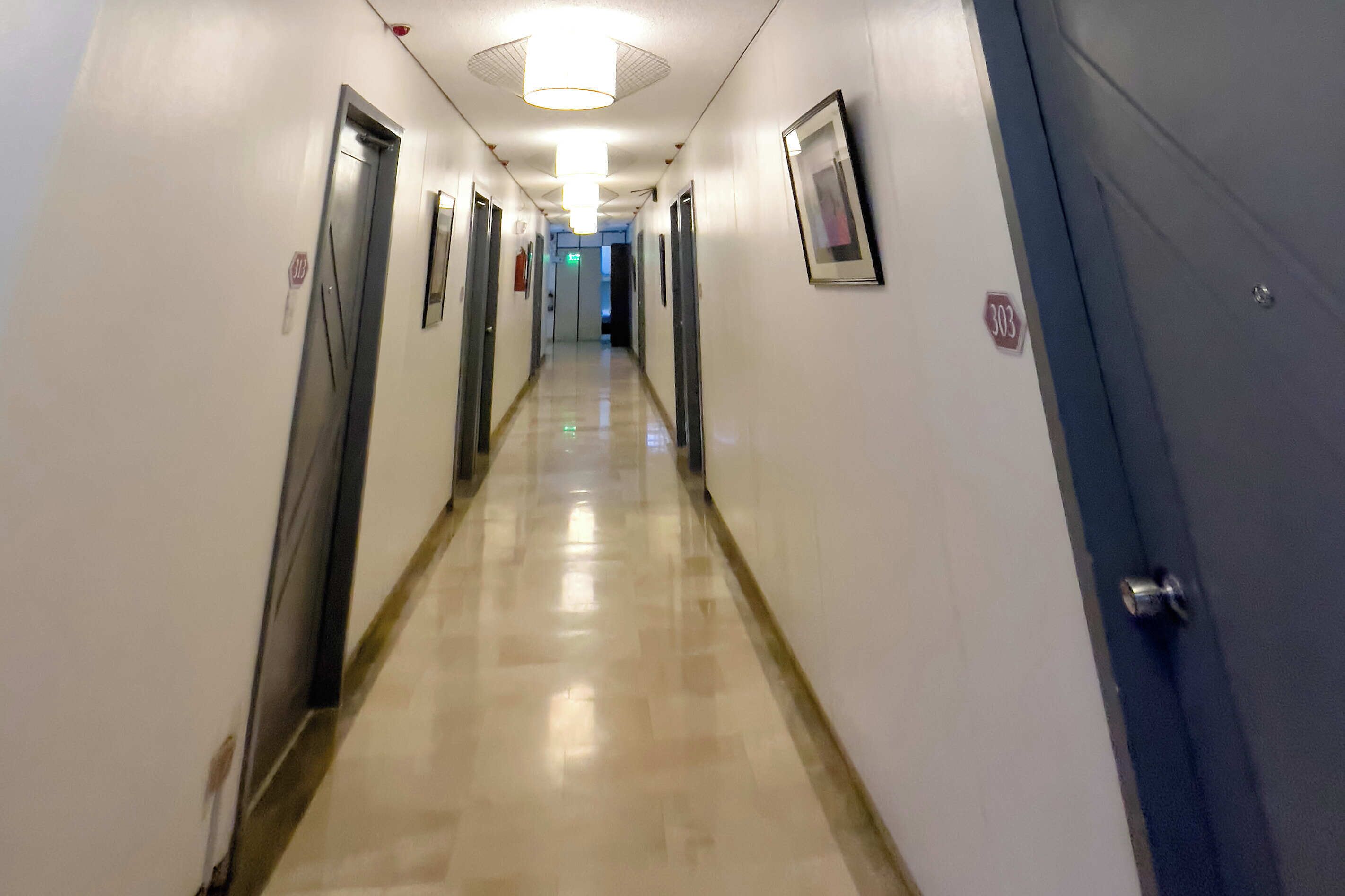 Pasillo de hotel con puertas a ambos lados, un accesorio de iluminación en el techo y una puerta con el número 303.