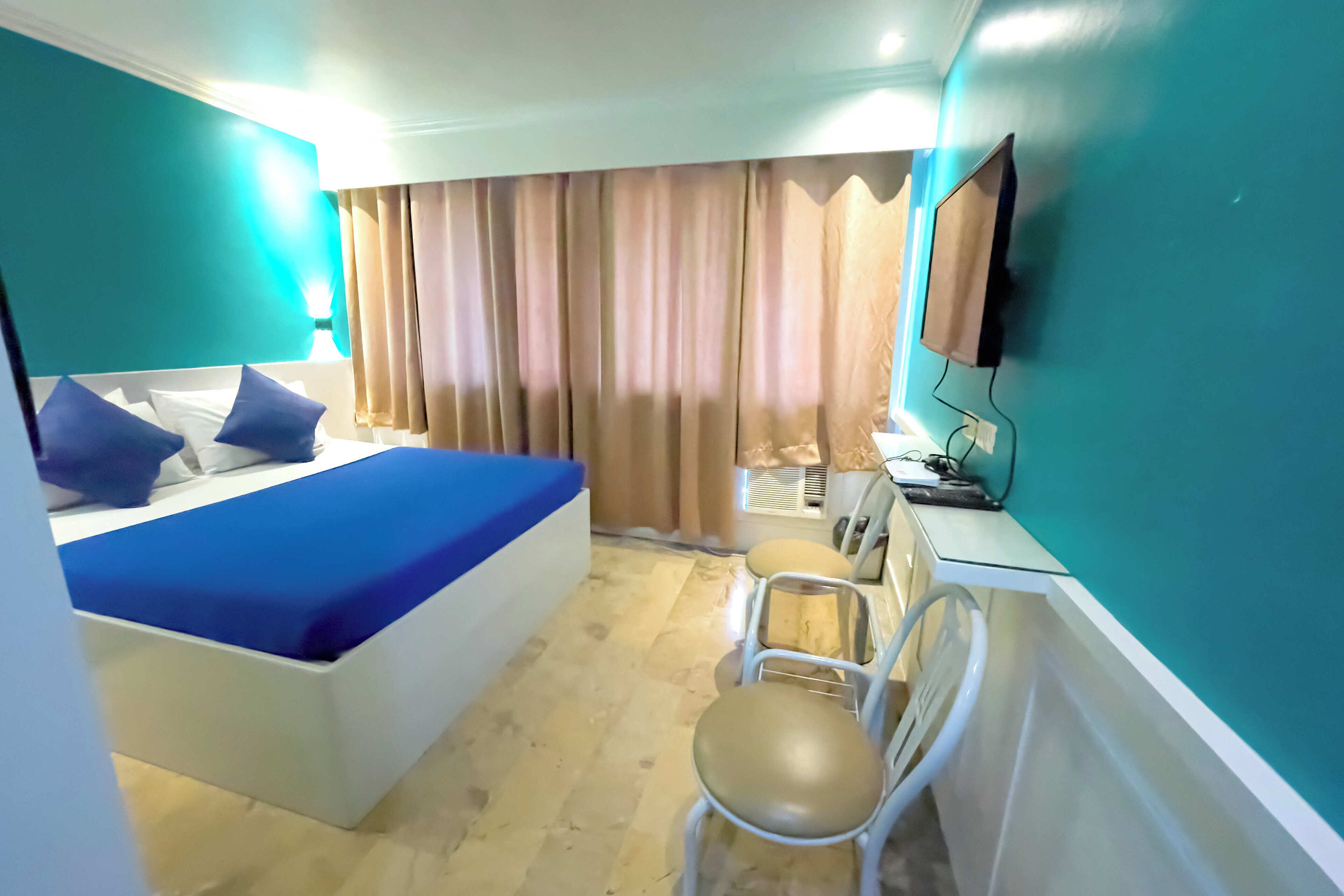Una habitación de hotel con cama, escritorio, silla, televisor y cortinas.