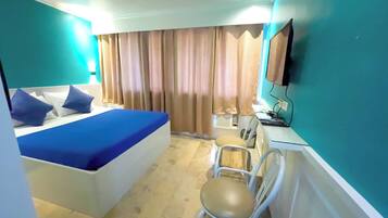 Una habitación de hotel con cama, escritorio, silla, televisor y cortinas.