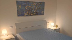 A bedroom with a bed, a nightstand, a lamp, and a painting on the wall. - The Carusians rent short (Marsala)