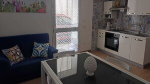 A compact kitchen with white cabinets, a black countertop, and a window with patterned curtains. - The Carusians rent short (Marsala)