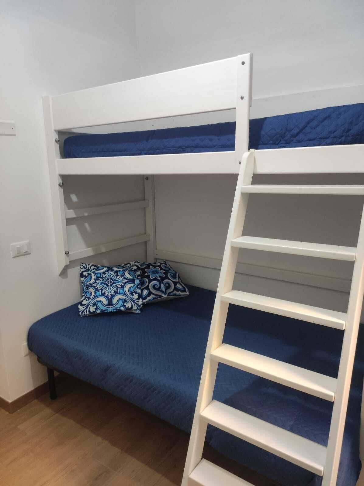 A bunk bed with a ladder, a blue mattress, and a patterned pillow.