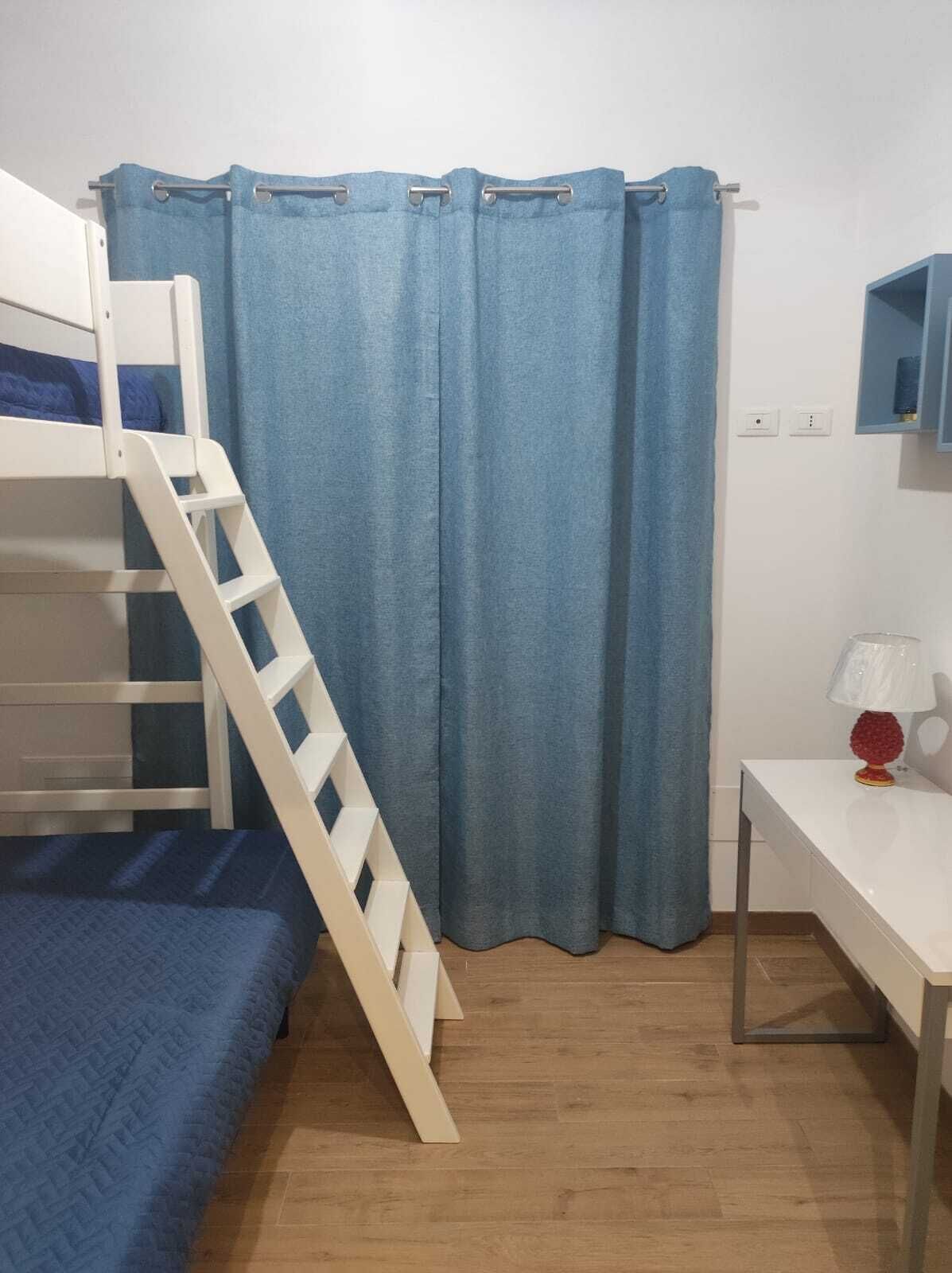 A bunk bed with a ladder, a desk with a lamp, and a blue curtain.