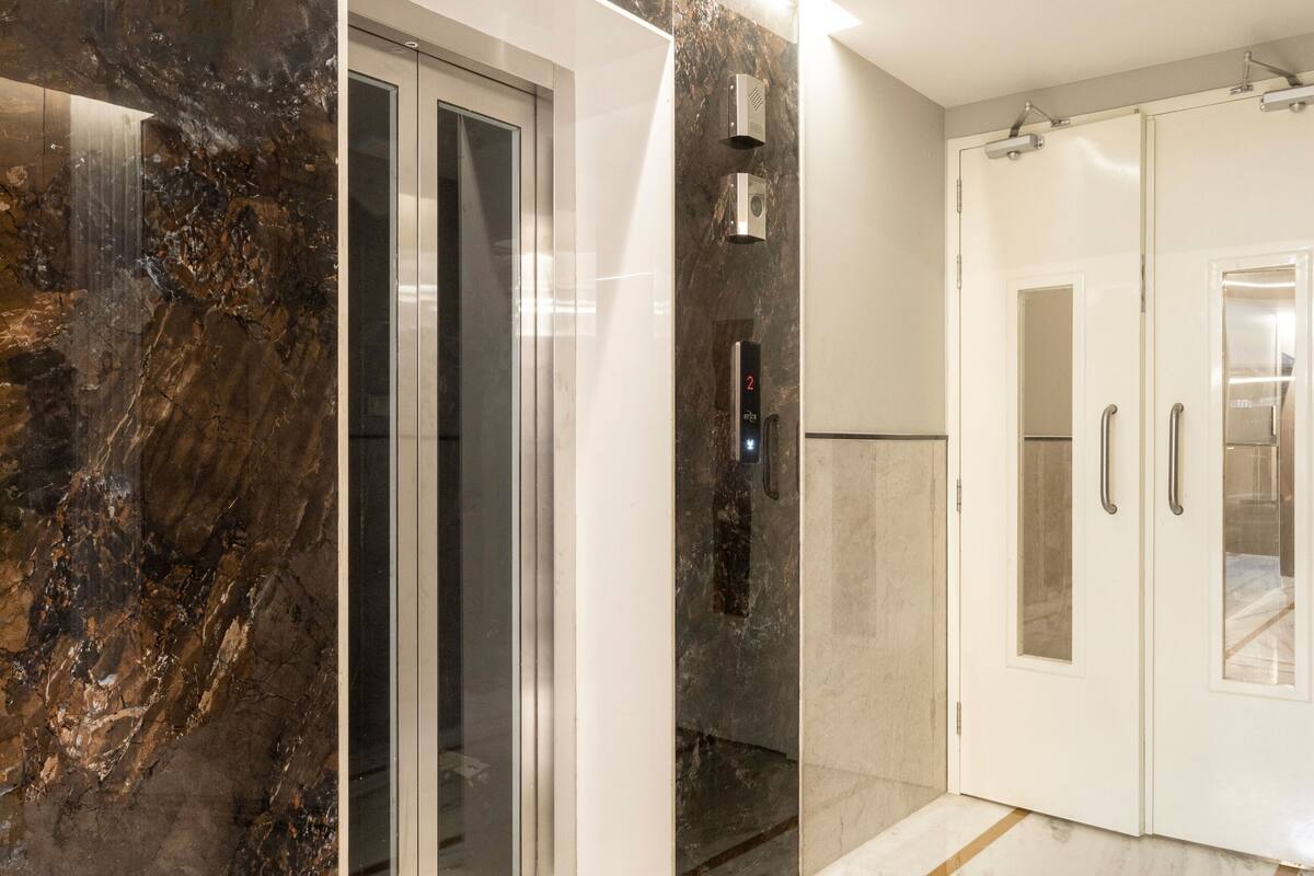 A modern elevator with a digital display, a glass door, and a marble wall.