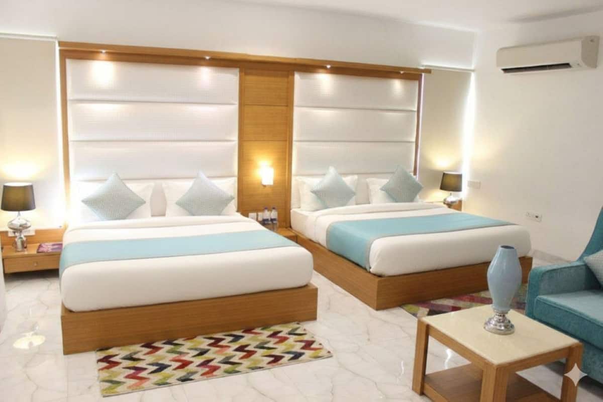 A hotel room with two beds, a small table, a chair, a rug, and a wall-mounted air conditioner.