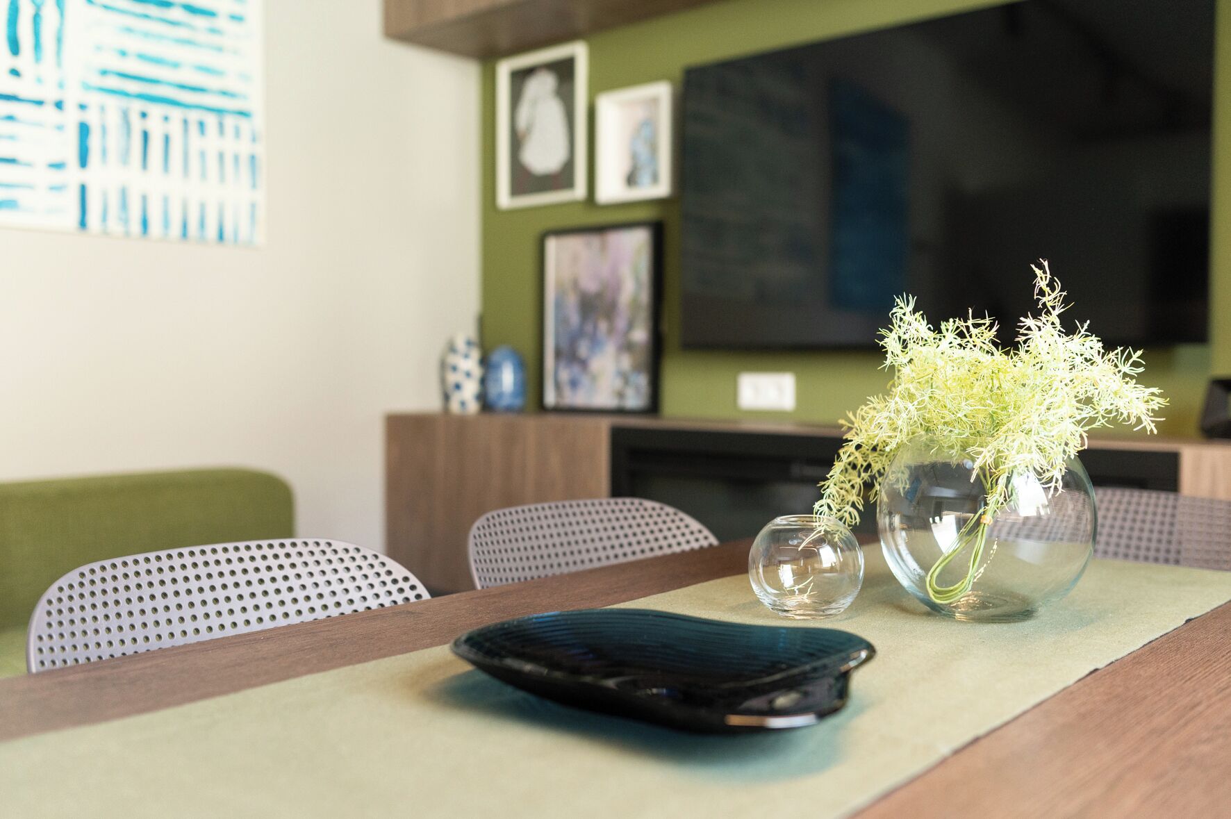 Een moderne woonkamer met een houten salontafel, een vaas met bloemen en een televisie aan de muur.