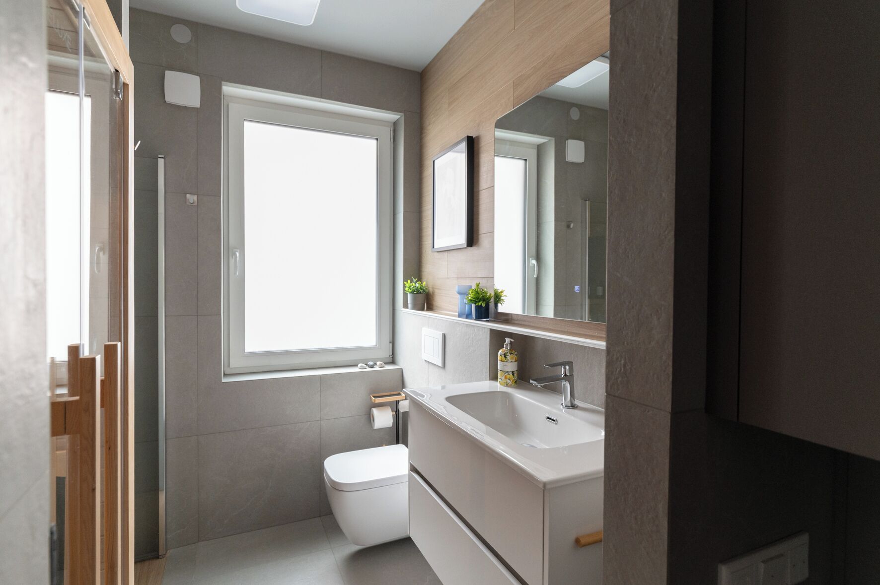 A modern bathroom with a large window, a toilet, a sink, and a mirror.