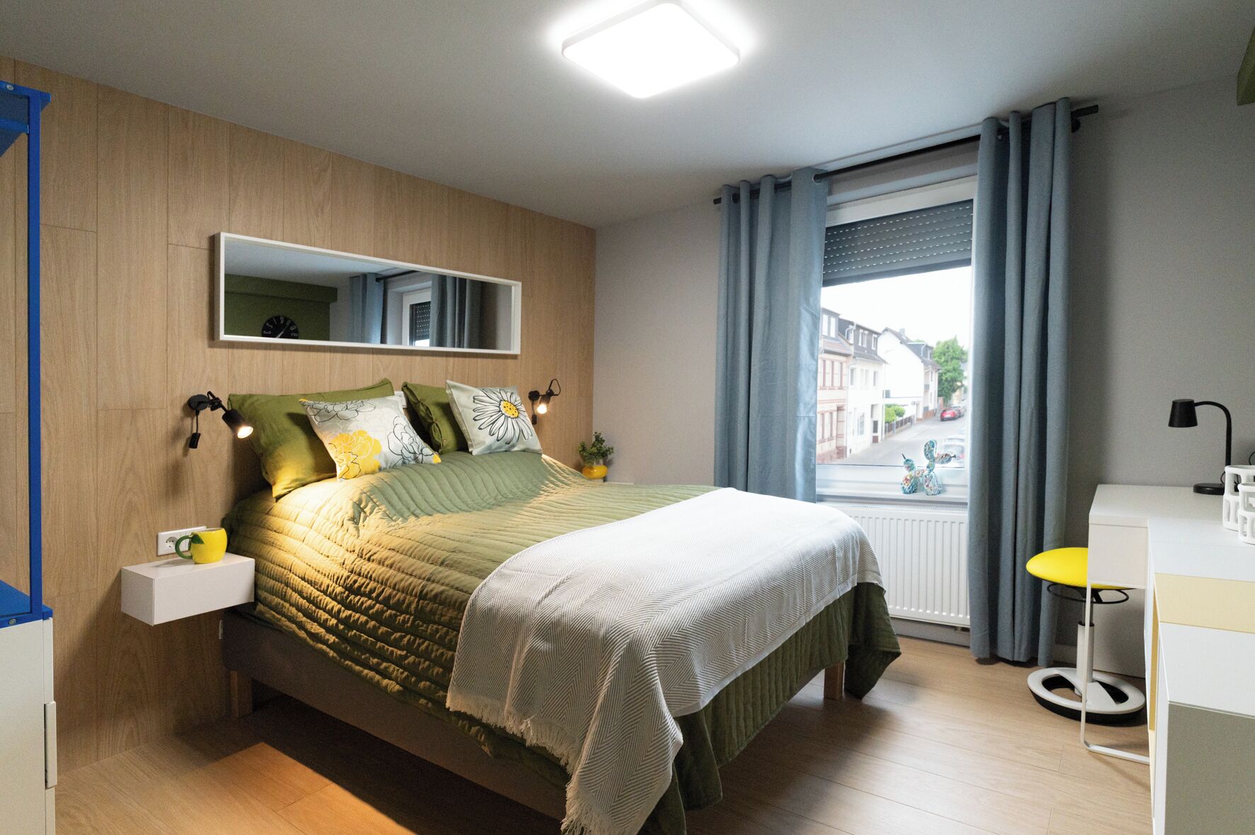 Ein modernes Schlafzimmer mit Bett, Nachttisch, Lampe und einem Fenster mit Vorhängen.