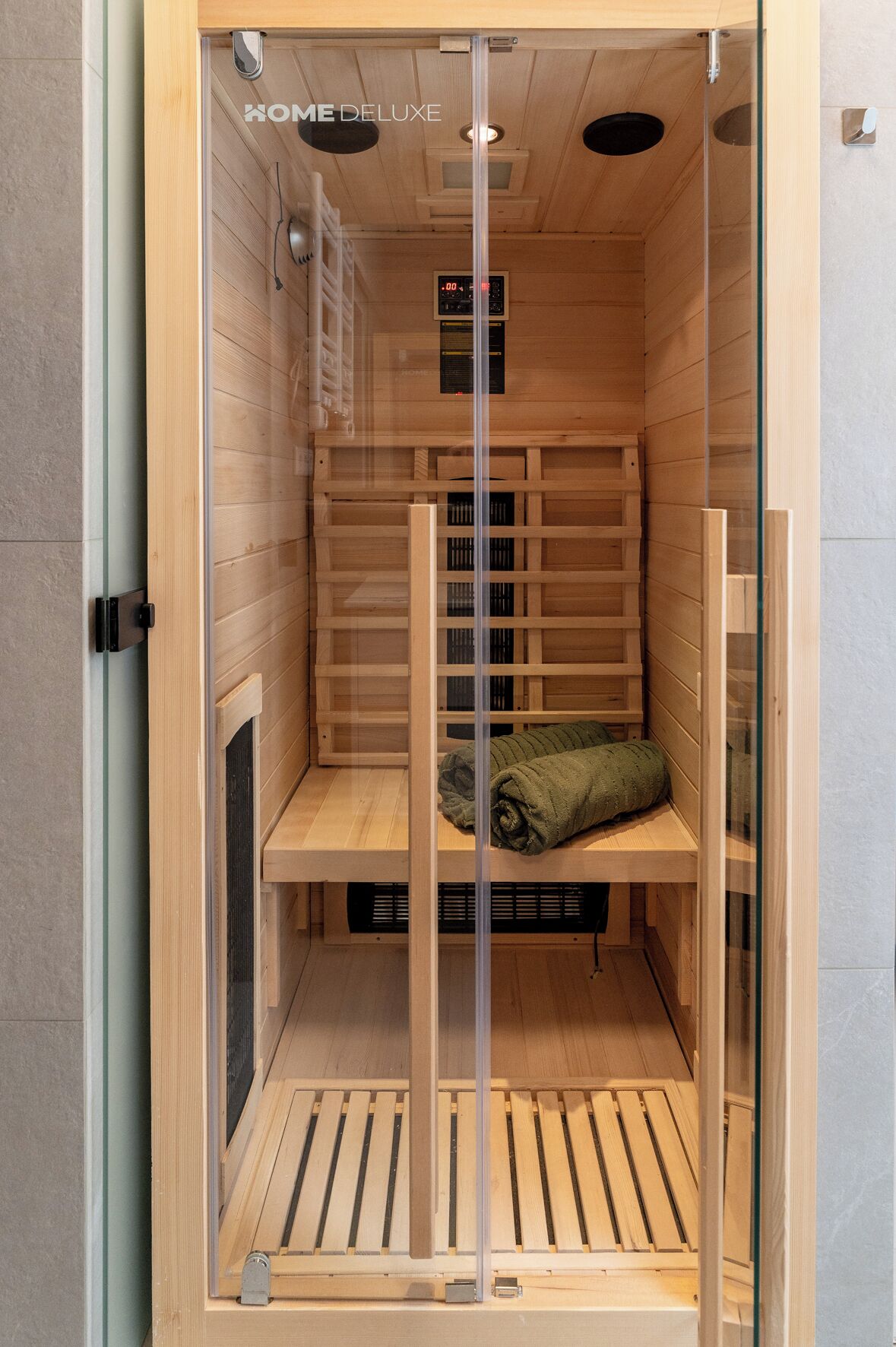A sauna with wooden walls, a digital timer, and a towel on the bench.