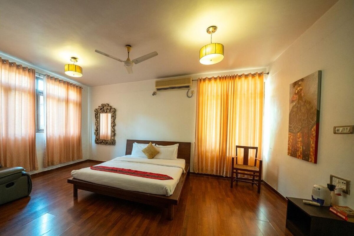 A hotel room with a wooden floor, a bed with white linens, a ceiling fan, and two wall-mounted lamps.