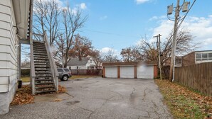 A garage with a car parked inside, a wooden fence, and a staircase leading to the garage. - TopUnit Floor Near Airport One bedroom (Cleveland)